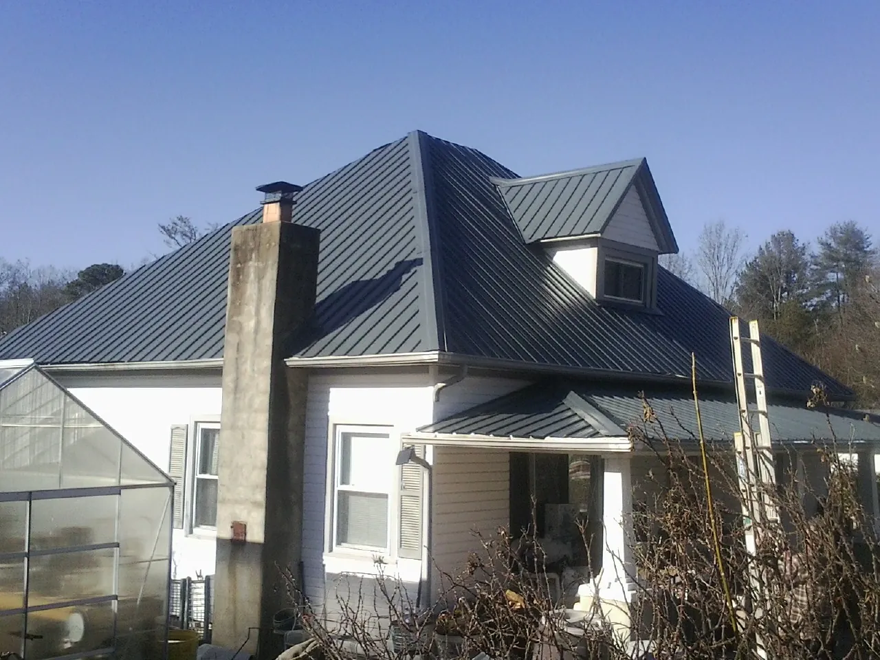 Dark blue standing seam metal roof on a white farmhouse with dormer — Slate & Tile Roof Repair by Roofing Brothers in Sayre