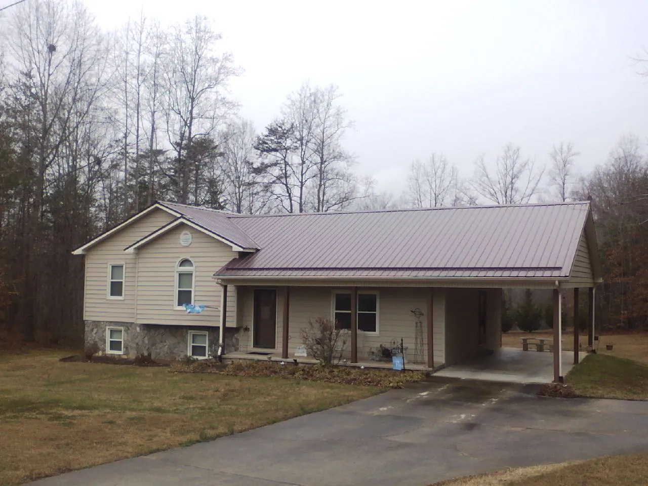 Burgundy metal roof on a tan split level home with an attached carport in Sayre