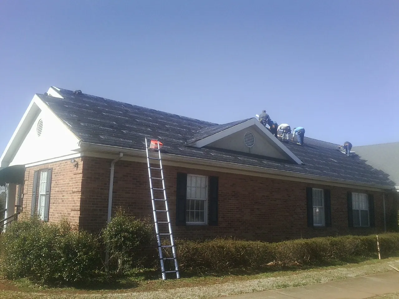 Crew tearing shingles off a brick ranch roof with a ladder set — Emergency Roof Repair work by our crew in Sayre