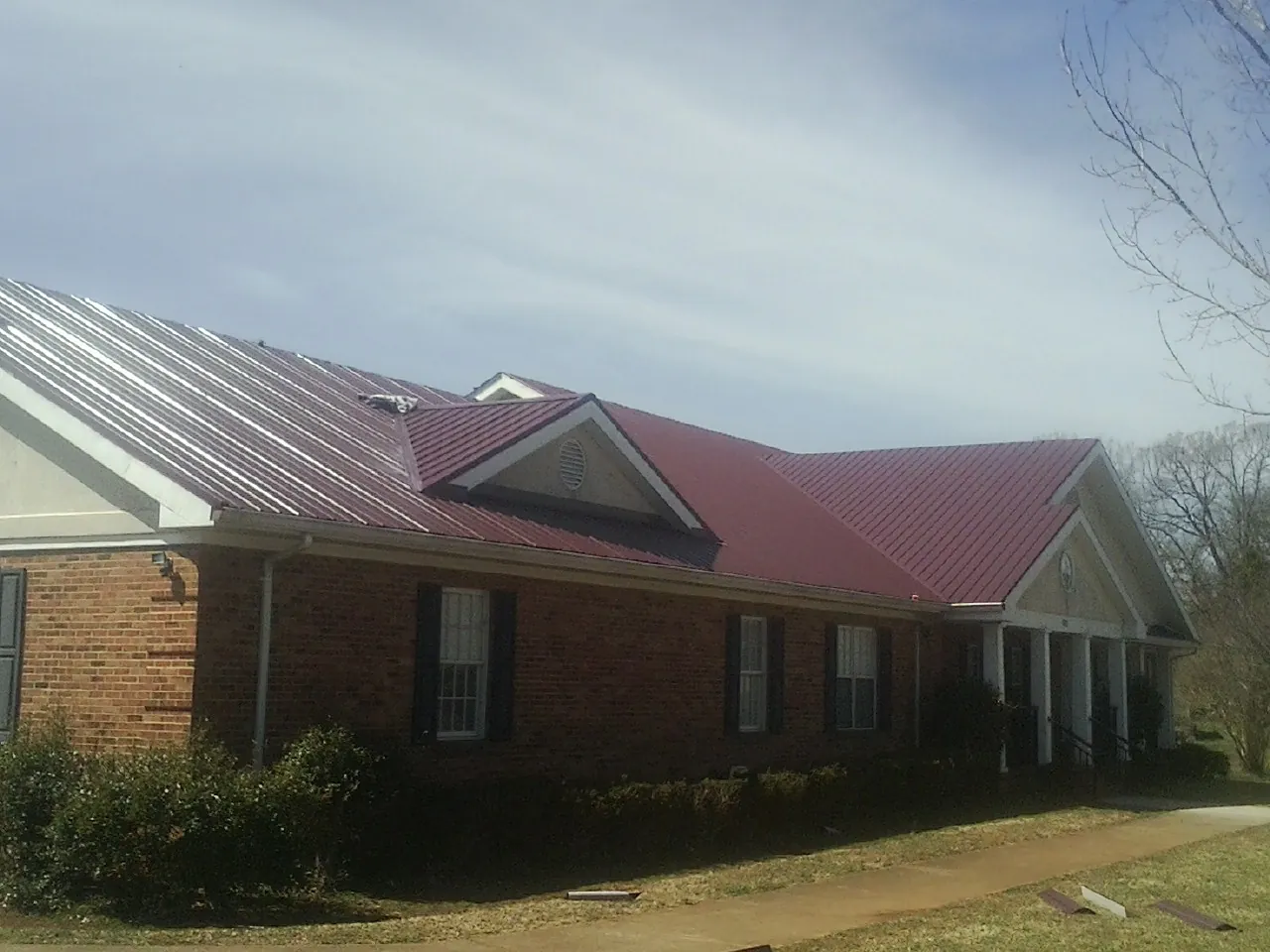 Red metal roof with gabled entries on a long brick building, from a Hail Damage Roof Repair job in Sayre