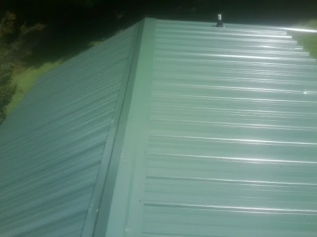 New green metal panels meeting at the ridge of a roof — Flat Roof Repair work by our crew in Sayre