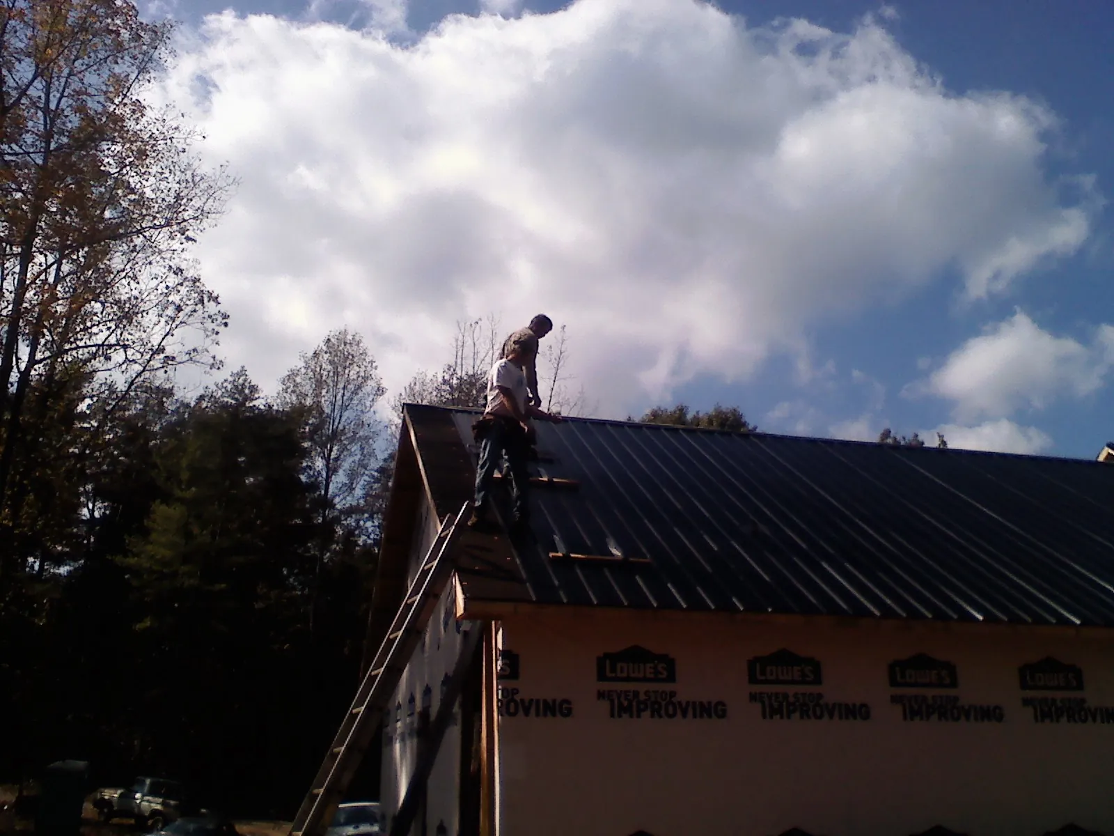 Roofer fastening dark metal panels high against a cloudy sky, from a Roof Inspection job in Sayre