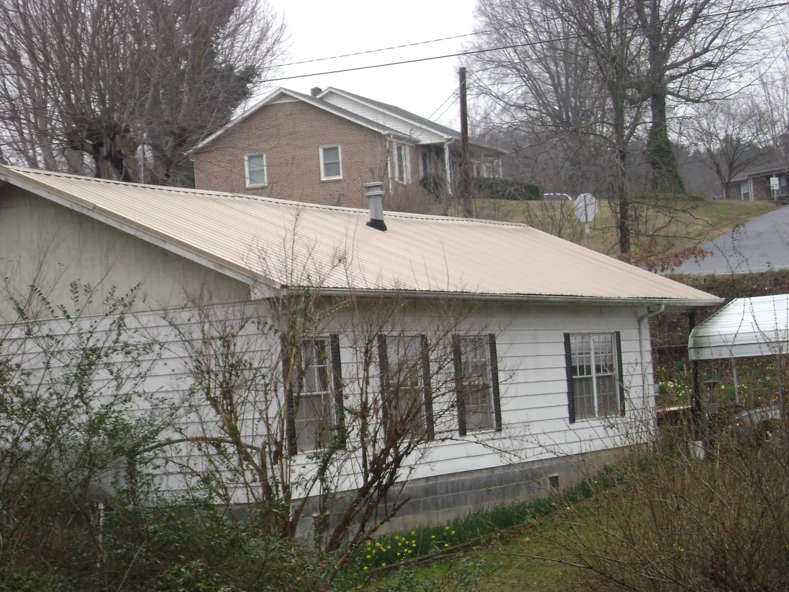 Tan metal roof on a white sided house set into a hillside — Commercial Roofing by Roofing Brothers in Sayre
