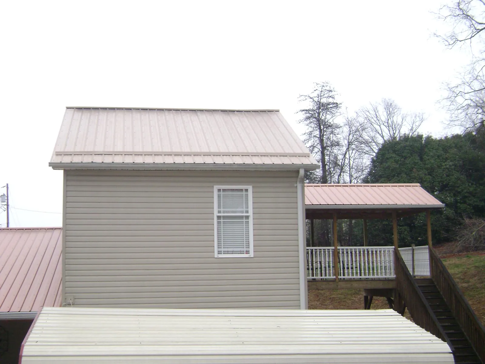 Tan metal roofs on a two story addition and attached porch, from a Roof Replacement job in Sayre
