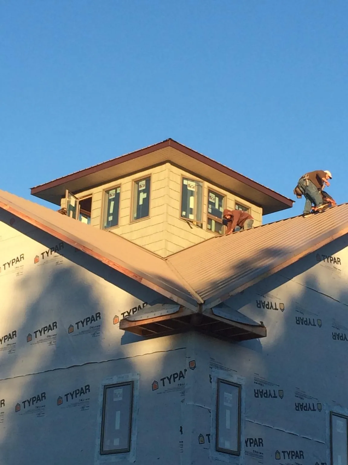 Roofers working around a rooftop cupola on a new metal roof at sunset — Roof Waterproofing in Sayre by Roofing Brothers